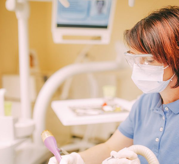 Zahnarzthelferin mit Mundschutz behandelt Patienten
